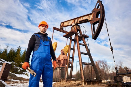 Portrait of oil well operator in protective helmet and work overalls holding industrial wrench. Male
